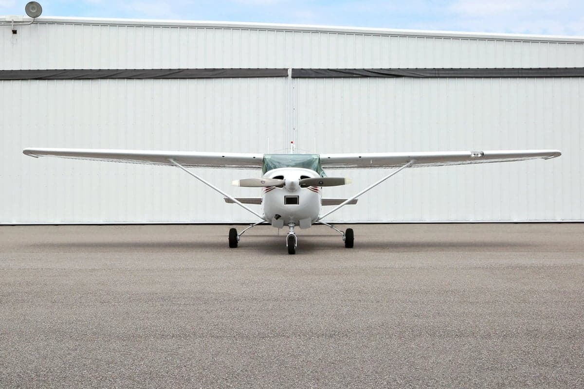 Front view of a Cessna aircraft with a white and red paint scheme parked in front of a hangar.