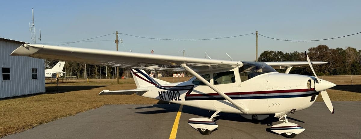 A white Cessna 210 Centurion, registration N71002, is parked on the tarmac.
