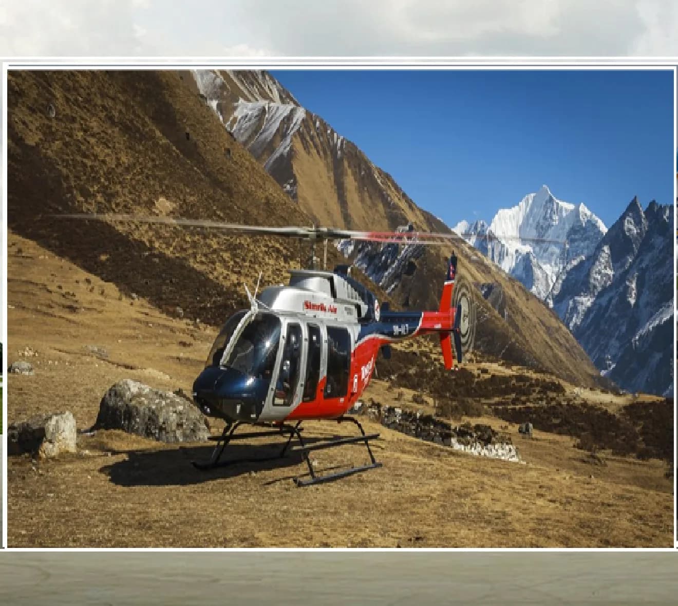 A red, white, and blue Simrik Air helicopter (9N-ALV) is parked on a rocky, dry terrain with snow-capped mountains in the background.