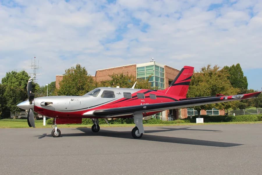 A Piper M600 aircraft, registration N501RL, in a red and silver paint scheme, parked on a tarmac with a building in the background.