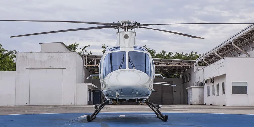 A white helicopter with gold stripes is parked on a blue helipad, viewed directly from the front.