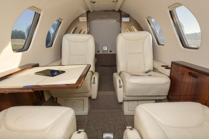 Interior view of the aircraft cabin with cream-colored leather seats and a table.