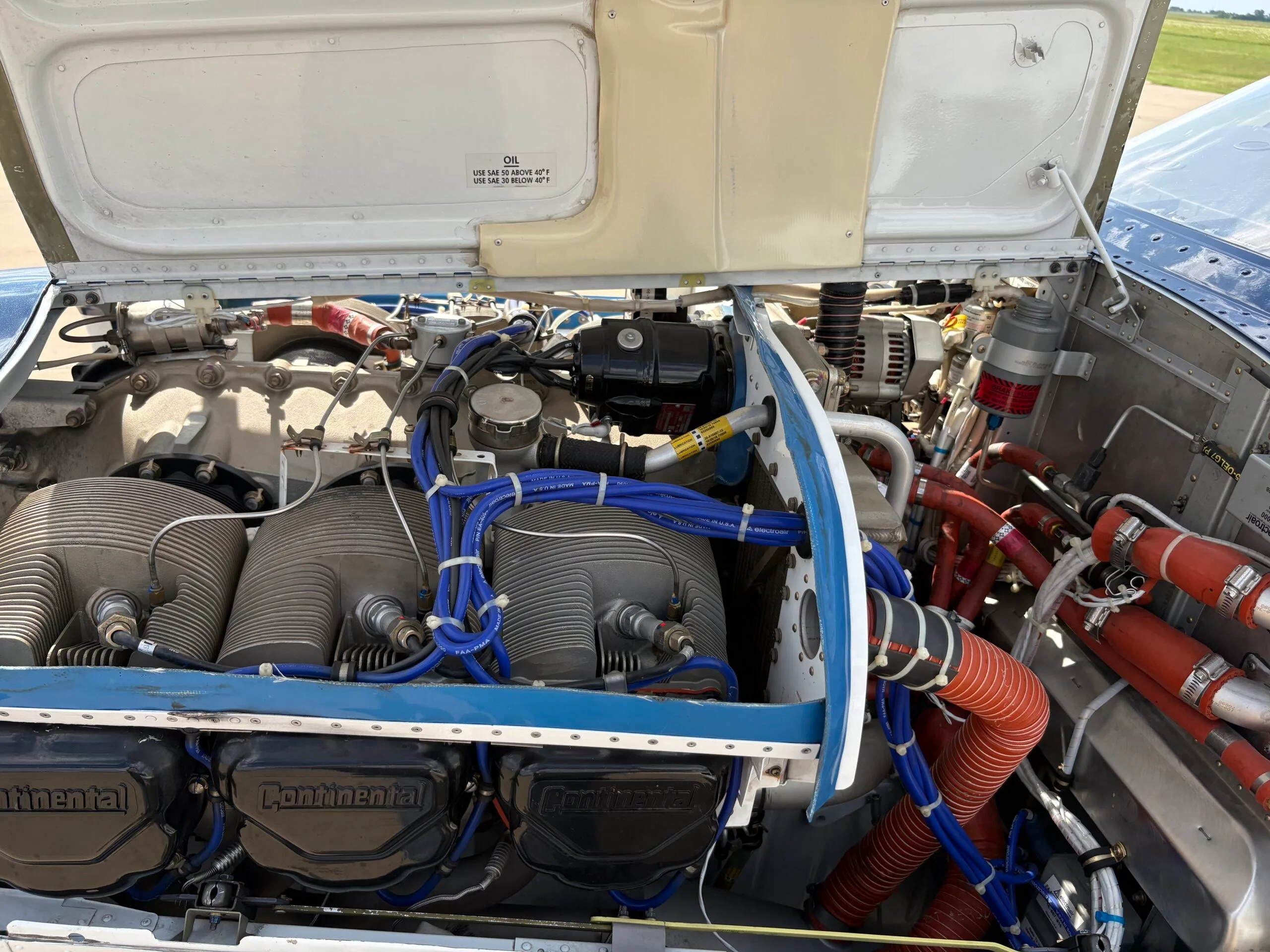 A detailed view of the open engine compartment of the Beechcraft Bonanza, showing the Continental engine cylinders and blue wiring.