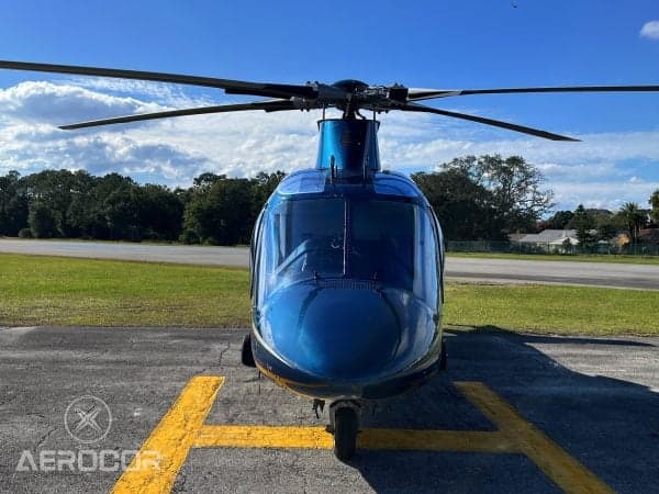 Front view of a blue AgustaWestland AW109 helicopter parked on an airfield under a blue sky.