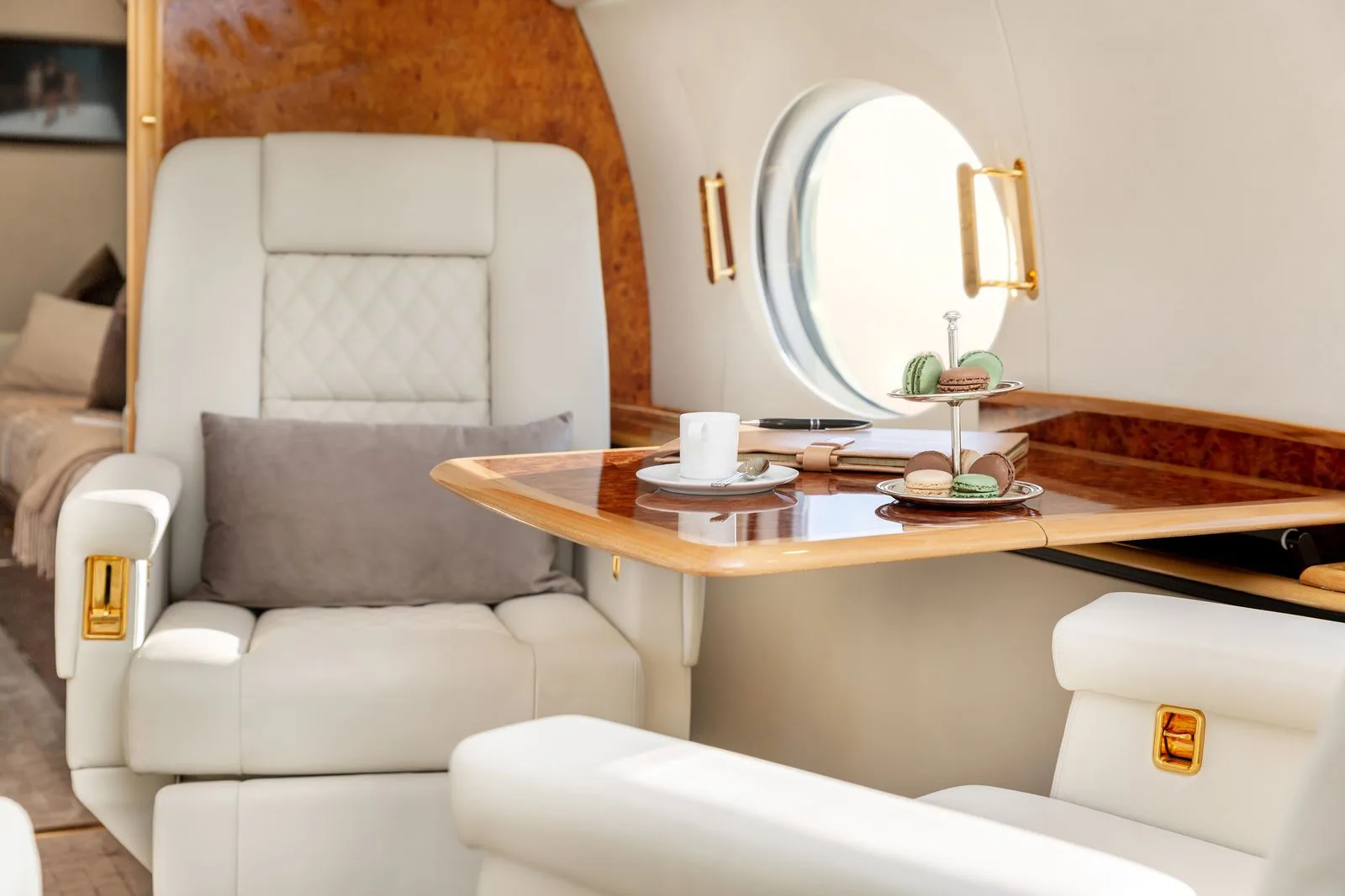 A luxurious aircraft interior with white leather seats, a wooden table, and a window.