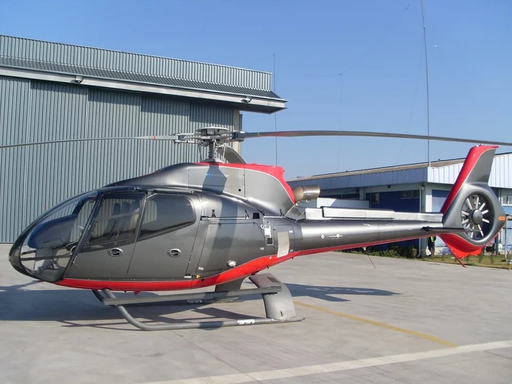Grey and red helicopter parked in front of a building.