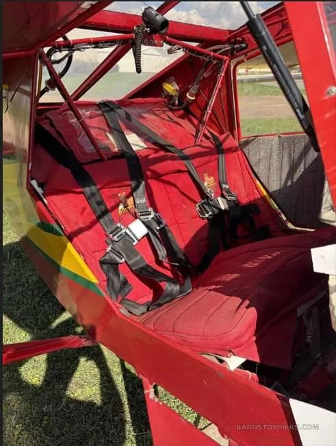 The red fabric seats and safety harnesses inside the open cockpit of an ultralight aircraft.