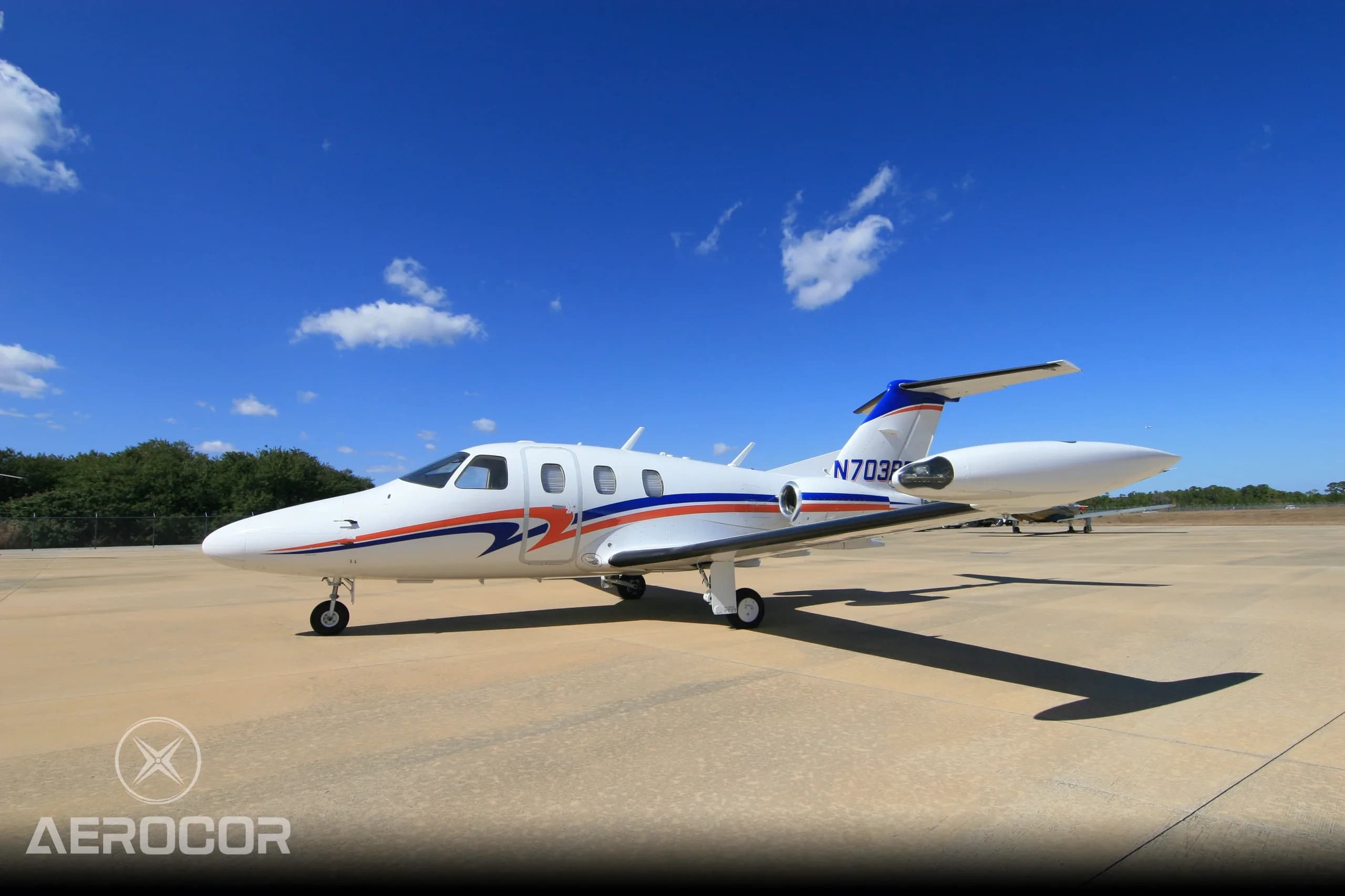 A front-side view of a white Eclipse 500 jet with blue and orange stripes, tail number N703BR, parked on an airfield.