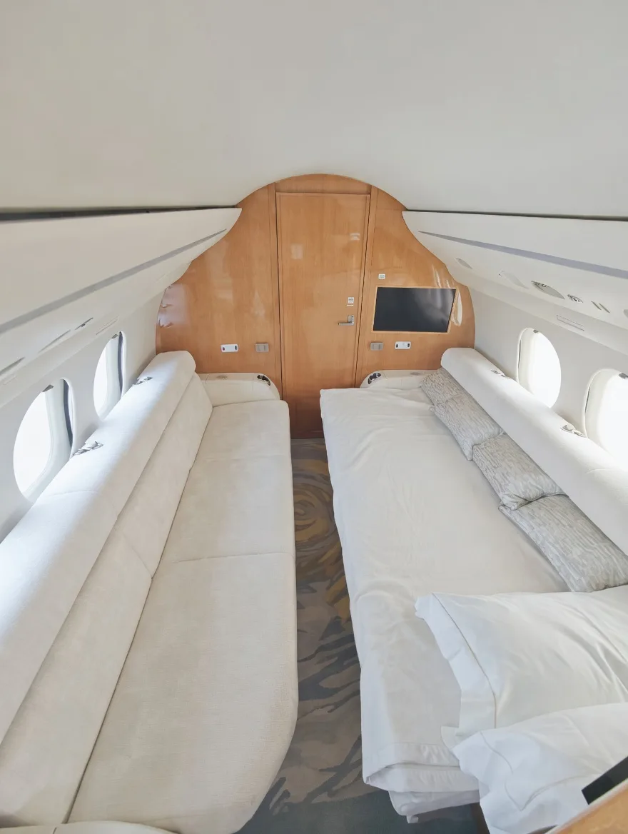 The aft section of an aircraft cabin configured with a long sofa and a bed, both in white upholstery.