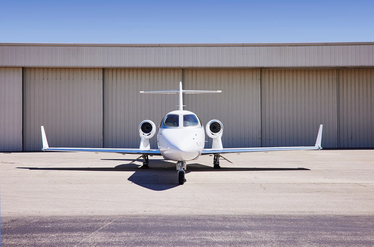 Front view of a white HondaJet in front of a hangar.