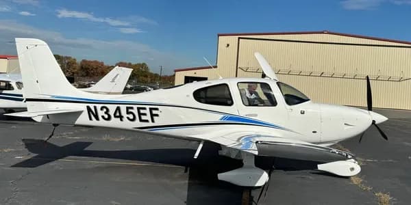 A white Cirrus SR20 aircraft with blue and black stripes, registration N700KP, parked on an tarmac.