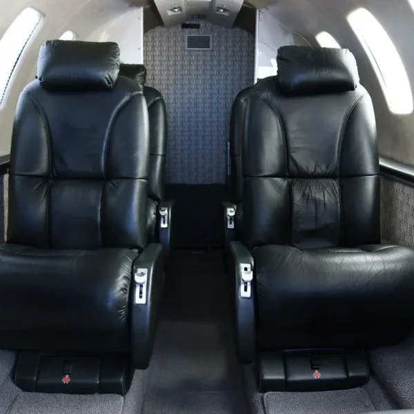 Interior view of a private jet cabin showing two rows of black leather seats.