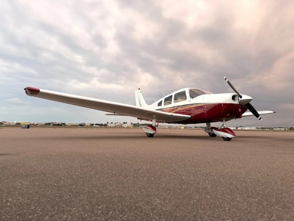 A white and maroon single-engine propeller aircraft is parked on an asphalt tarmac under a cloudy sky.