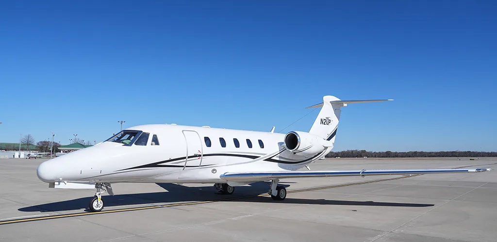 A white Cessna Citation business jet with black and grey stripes, registration N2UP, parked on an airfield.
