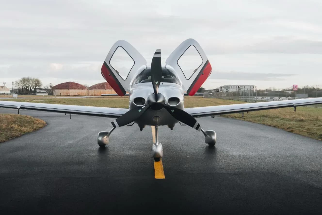 A silver and red Cirrus SR22 aircraft viewed from the front with its doors open, parked on an airfield.