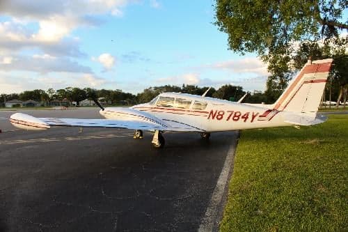 A white and red Piper aircraft, registration N8784Y, parked on the tarmac.