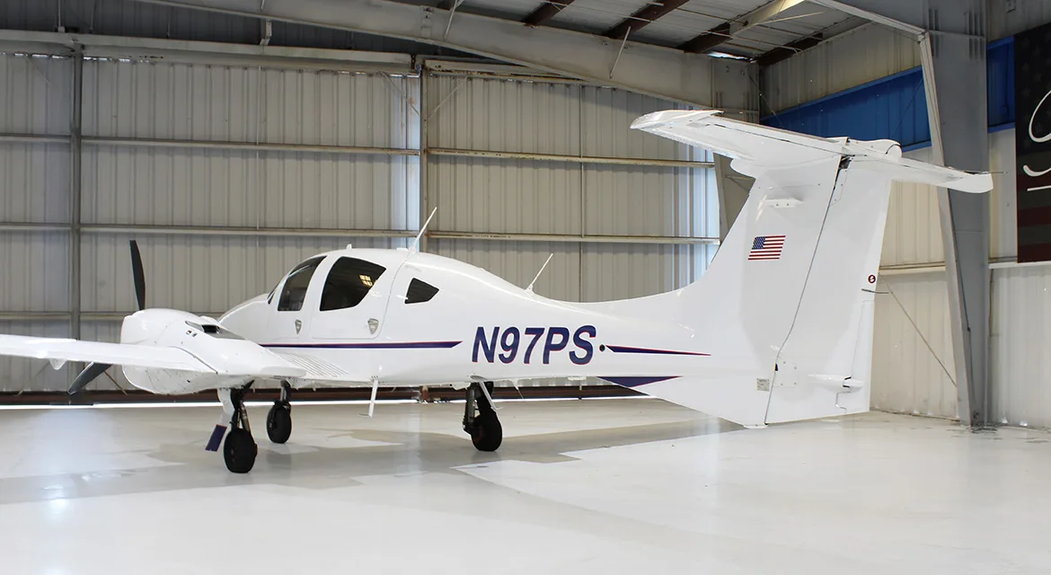 Rear quarter view of a Diamond DA62 aircraft with registration N97PS in a hangar.