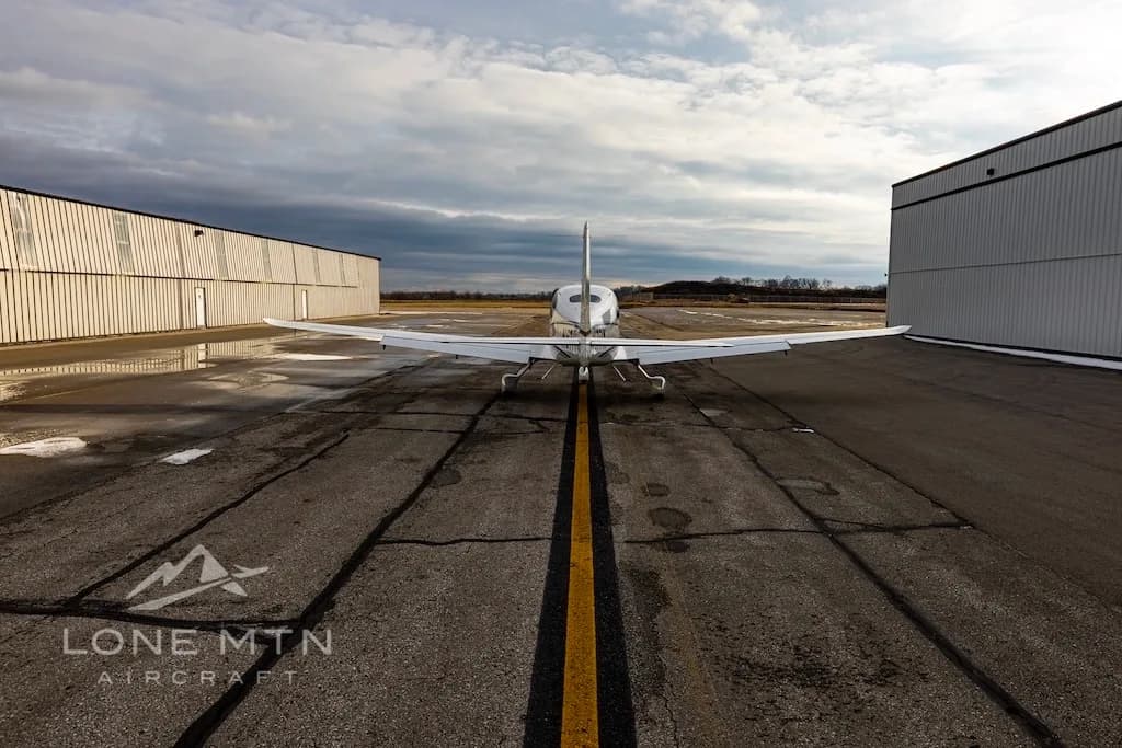 A rear view of a white Cirrus SR22 aircraft, tail number N57PX, parked between two hangars on an airport tarmac.