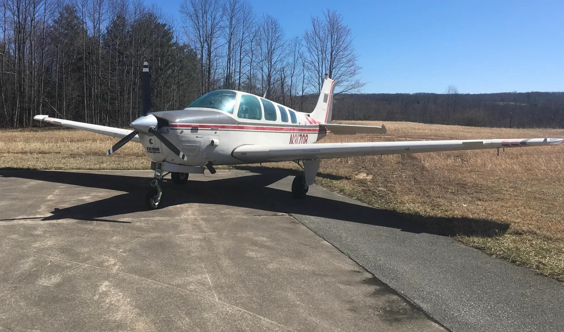 A wide front-quarter view of a white and red Beechcraft Bonanza N31708 parked on an asphalt ramp under a clear blue sky.