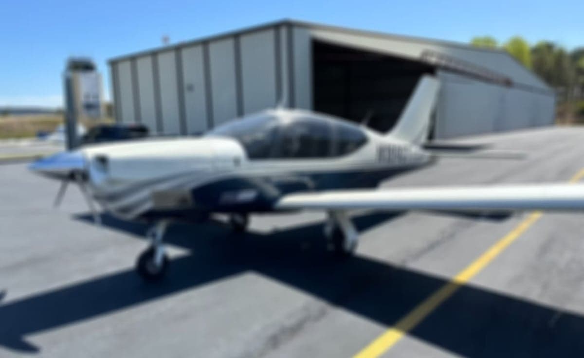 A blurry image of a Trinidad GT aircraft parked on the tarmac.