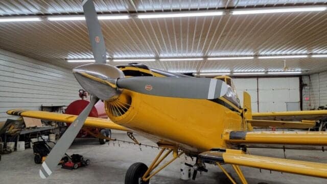 Side view of a yellow and black aircraft with a lawnmower in the foreground.