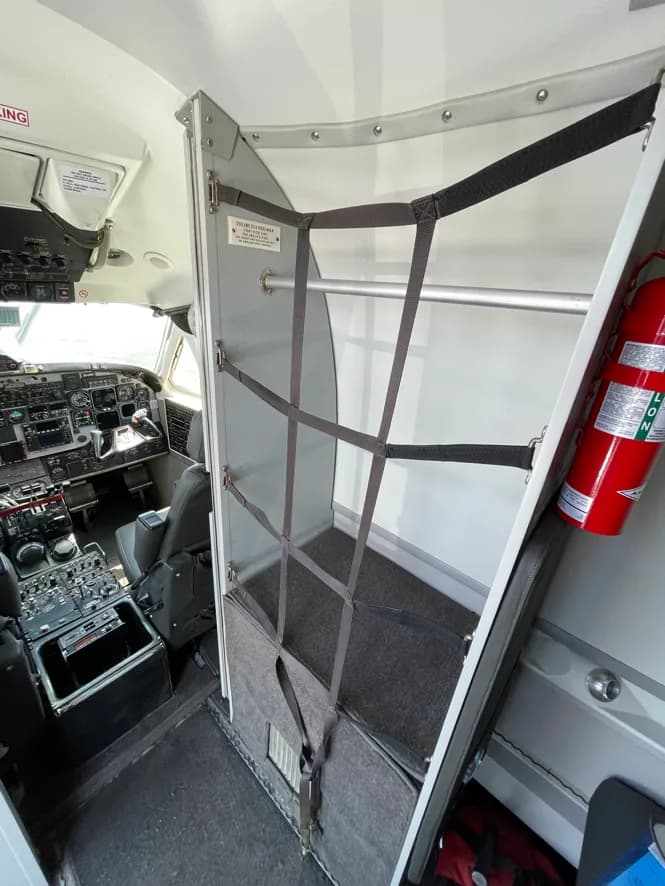 A view from the cockpit area showing a storage unit with netting and a fire extinguisher, with the instrument panel visible on the left.