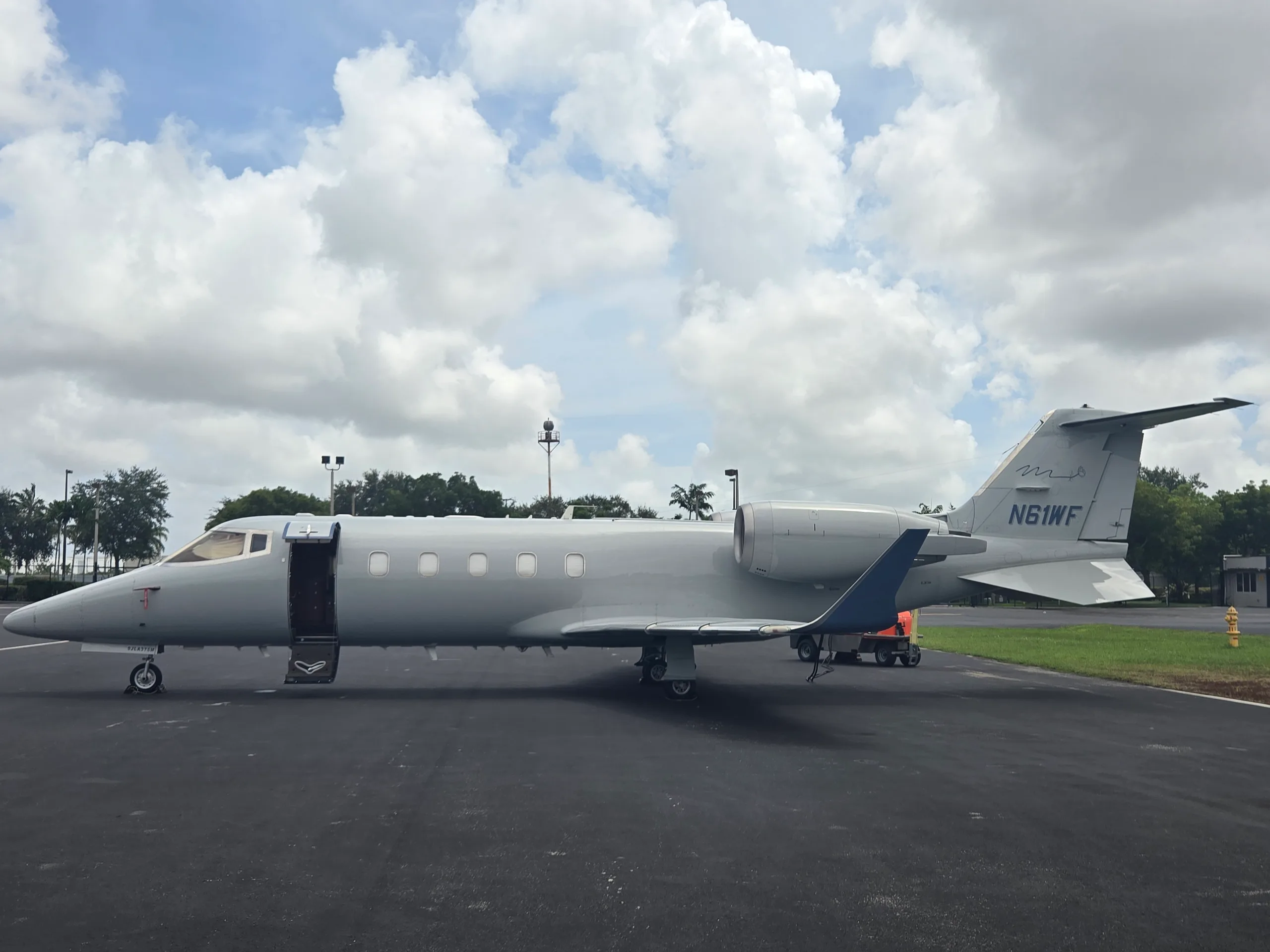 A Learjet business jet, registration N61WF, in a light gray paint scheme, parked on an asphalt tarmac with its main door open.