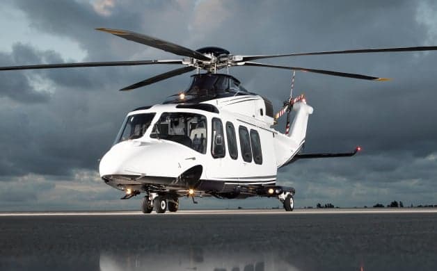 A white and blue helicopter on a reflective surface at sunset.