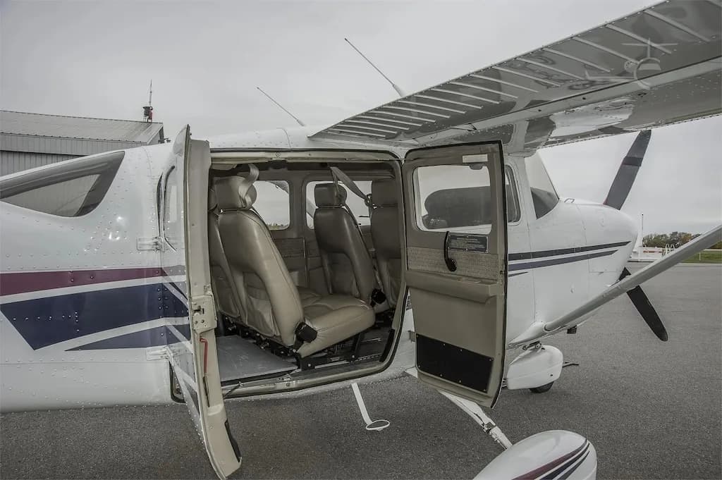 The open doors of a white single-engine propeller aircraft reveal its tan leather cabin seats.