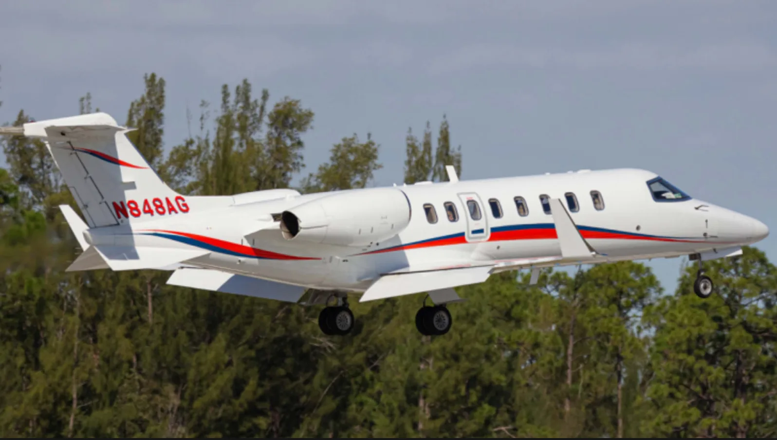 A white Learjet 45XR with red and blue stripes is shown in flight.