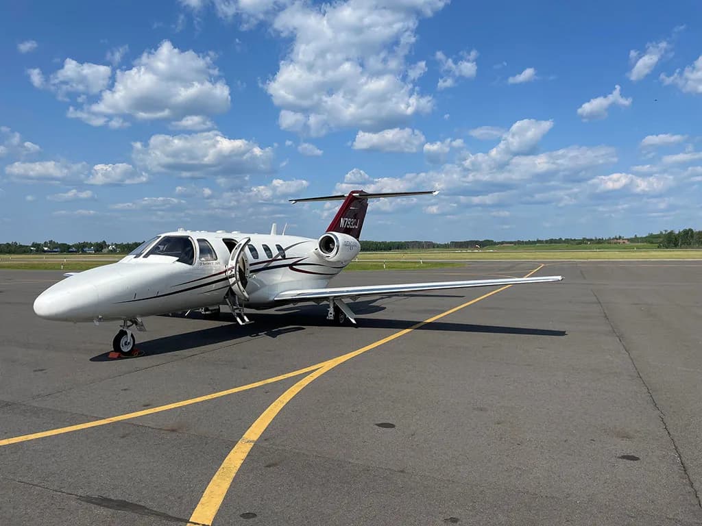 A white Cessna Citation CJ1 private jet with its main cabin door open, parked on an airport tarmac.