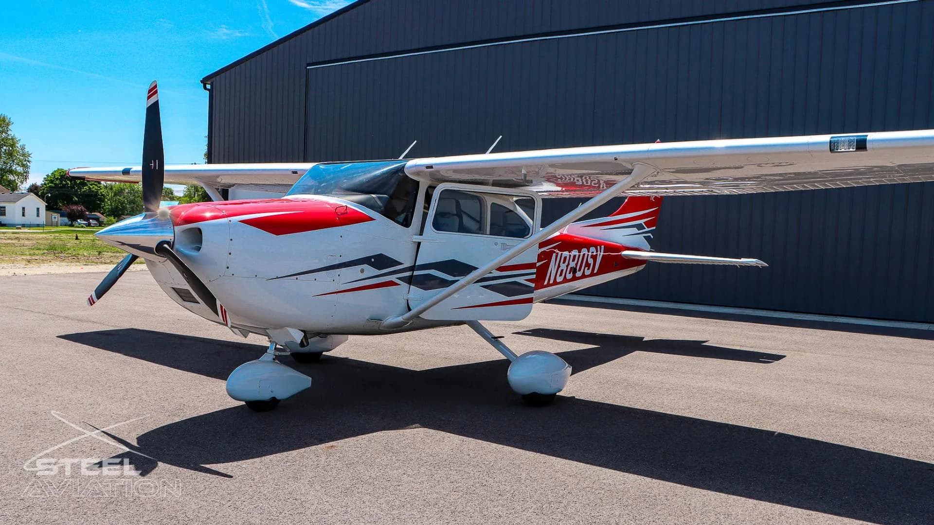 A side view of a white Cessna T182T Skylane TC with red and grey stripes, tail number N880SV, parked on an asphalt tarmac.