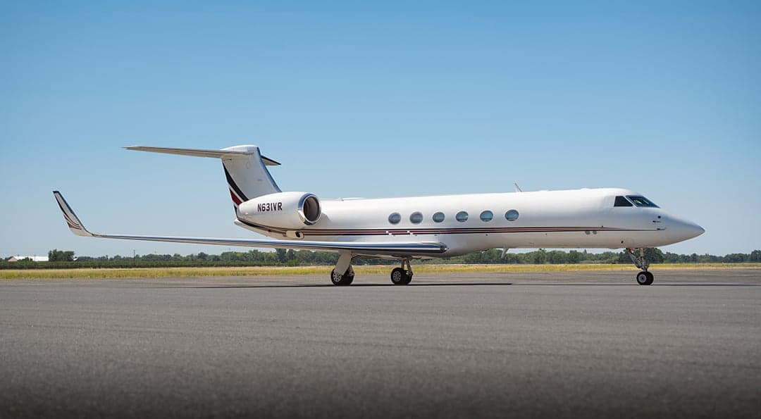 A white Gulfstream G550 business jet with a red and black stripe on the tail, registration N631VR, parked on an airfield, viewed from the front-right.