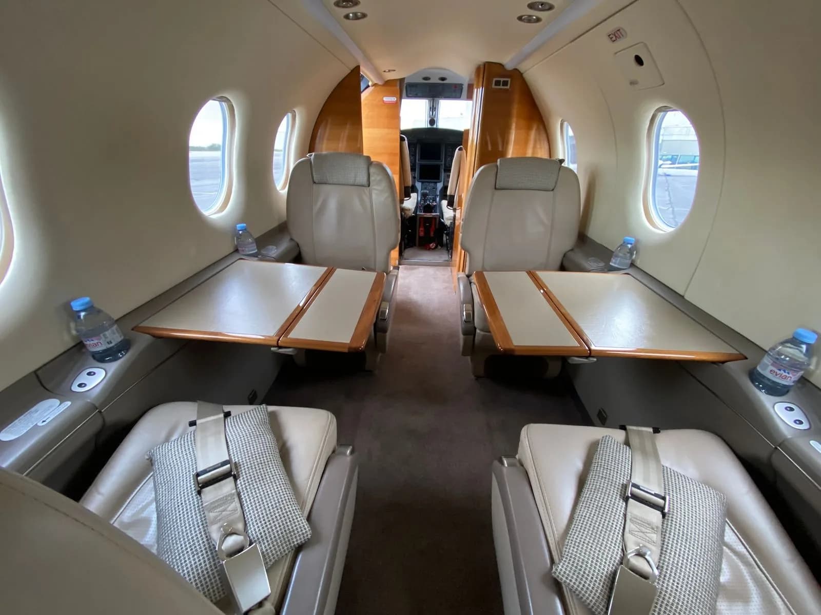 The interior cabin of a Pilatus PC-12 NG, showing beige leather seats with fold-out tables and a view towards the cockpit.