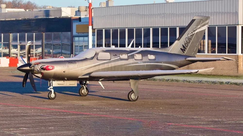 A Piper M600 HALO aircraft parked on the tarmac in front of a building on a sunny day.