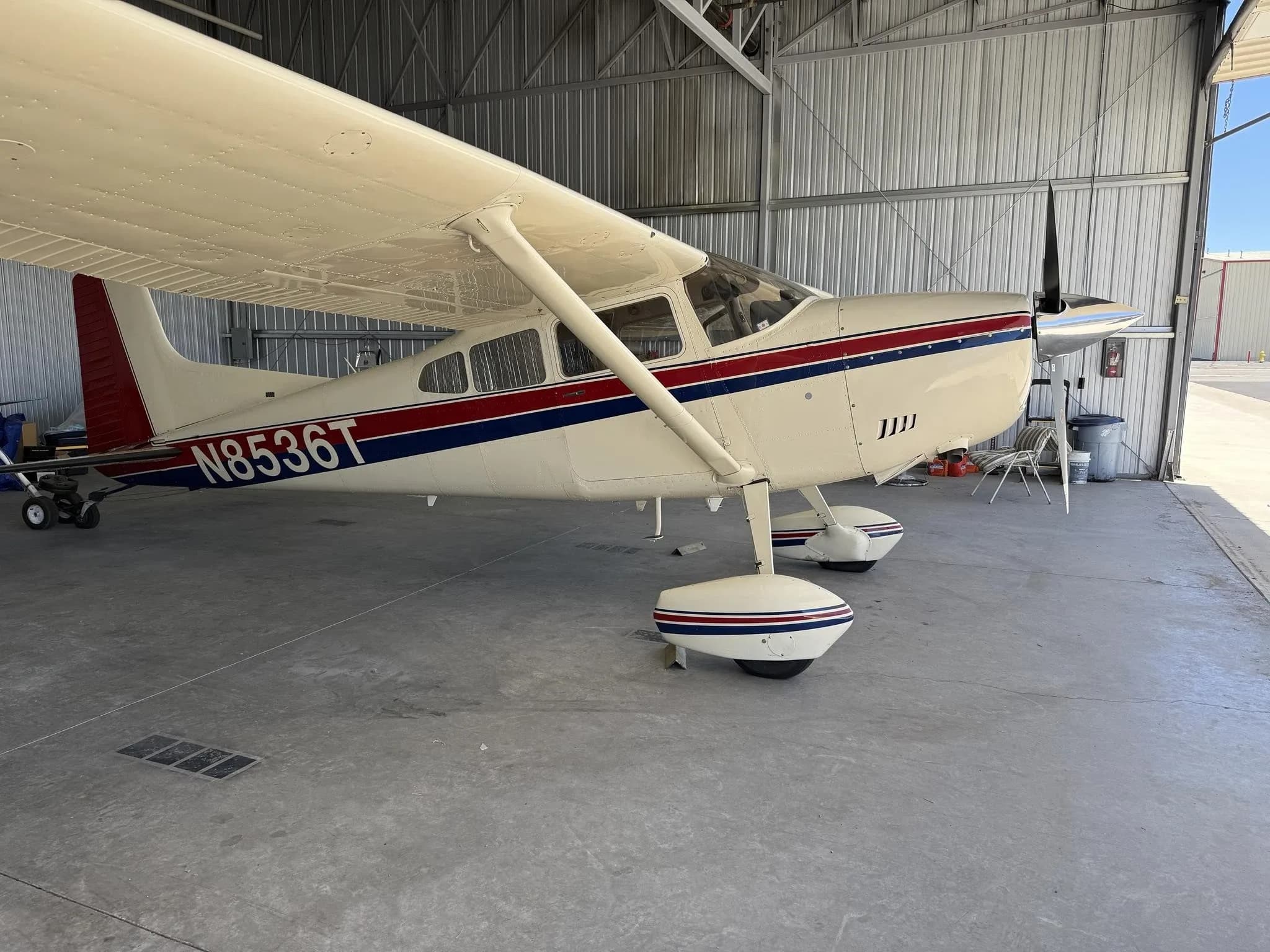 A white Cessna aircraft with red and blue stripes, registration N8536T, parked in a hangar.