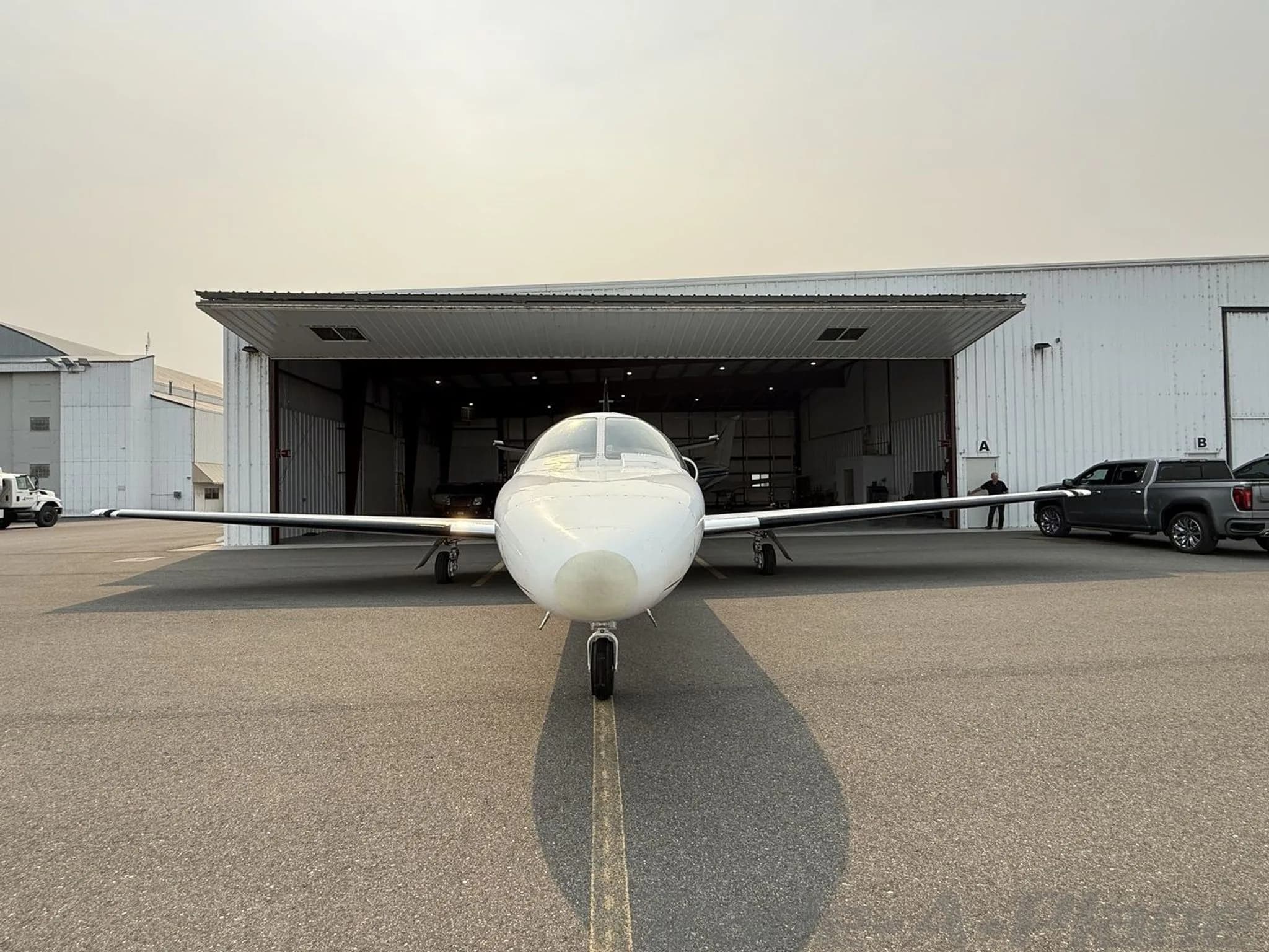 A white Cessna Citation jet, N90JJ, seen from the front, parked on an tarmac in front of an open hangar.