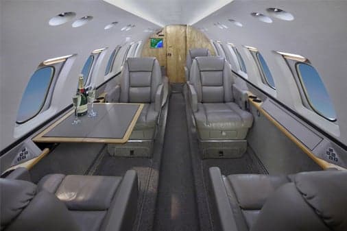 The interior cabin of a private jet with grey leather seats, a table, and champagne.