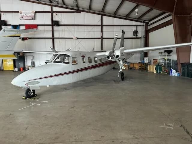 A front-side view of a white and red Aero Commander 680FL twin-engine aircraft, registration N199WM, parked in a hangar.
