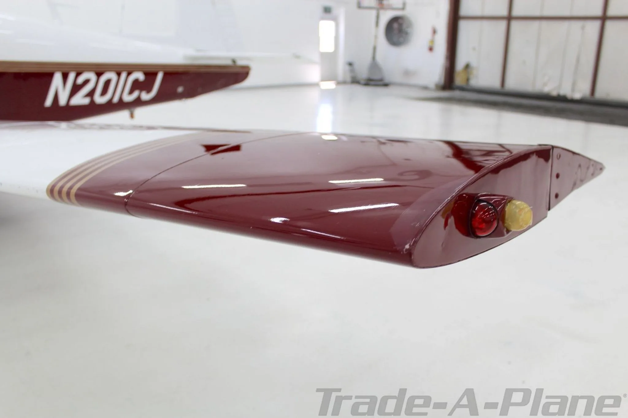A close-up view of the maroon wingtip of the Mooney M20J, N201CJ, featuring navigation lights.