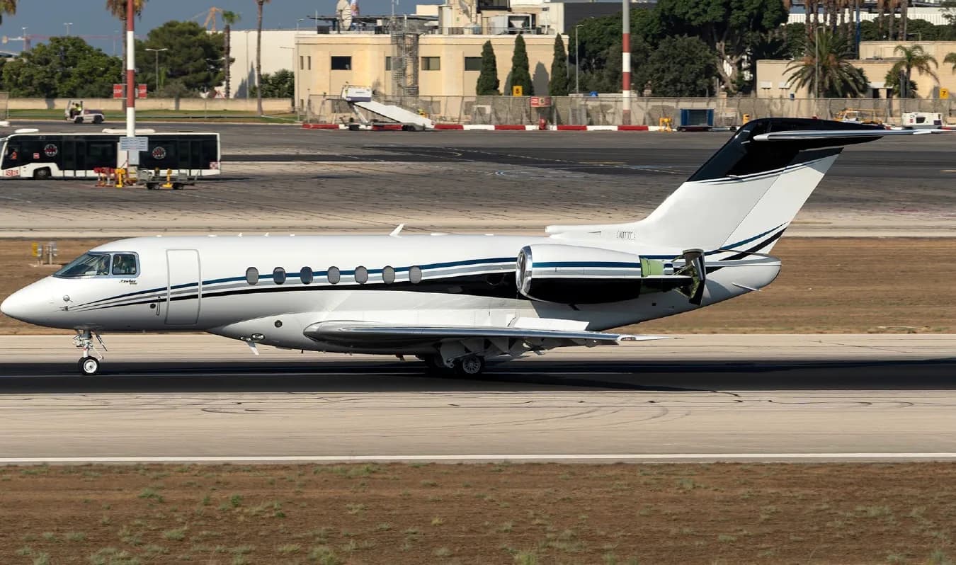 A white and black business jet is shown on the runway with its thrust reverser deployed.
