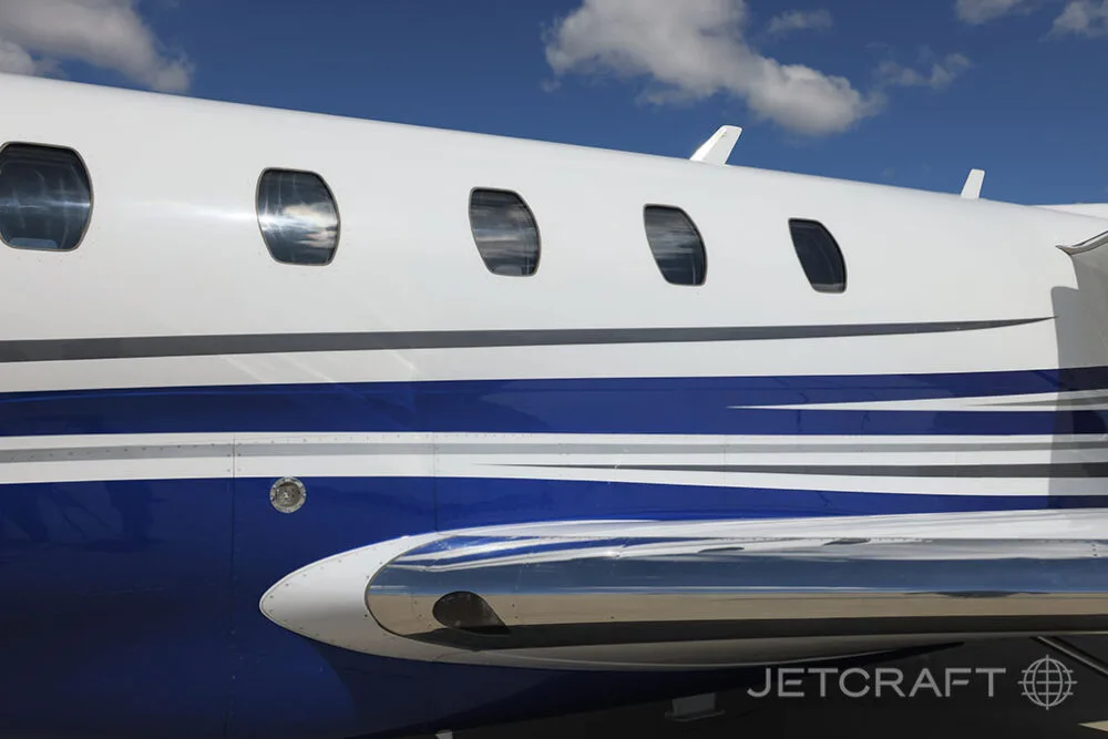 A close-up view of the white and blue fuselage and polished wing leading edge of a Cessna Citation X.