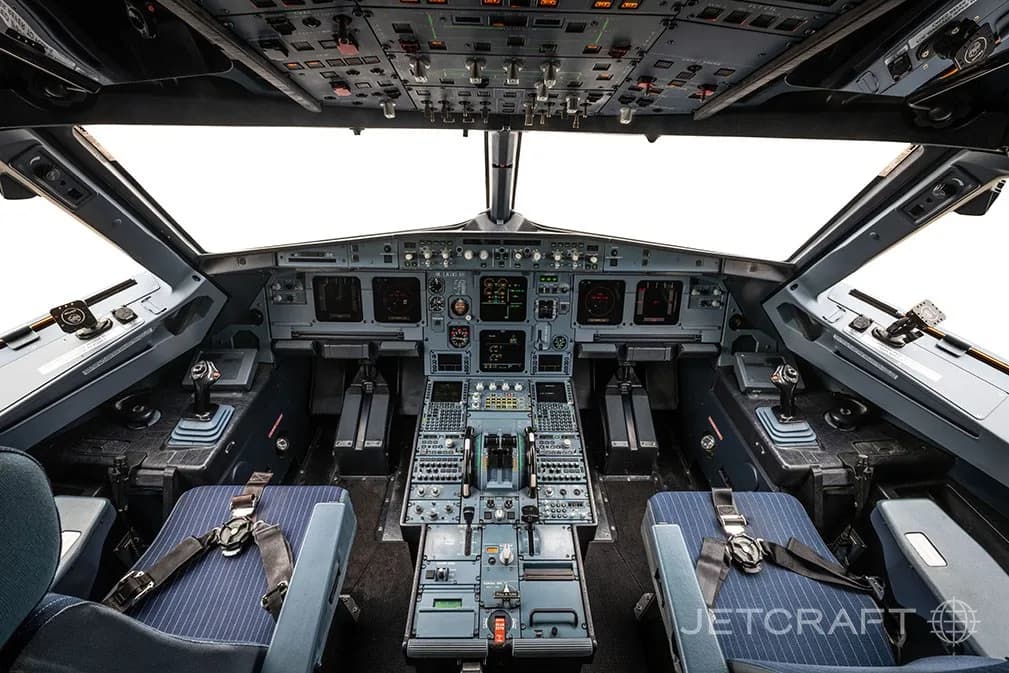 The detailed cockpit of an Airbus A320 family aircraft with multiple screens and controls.