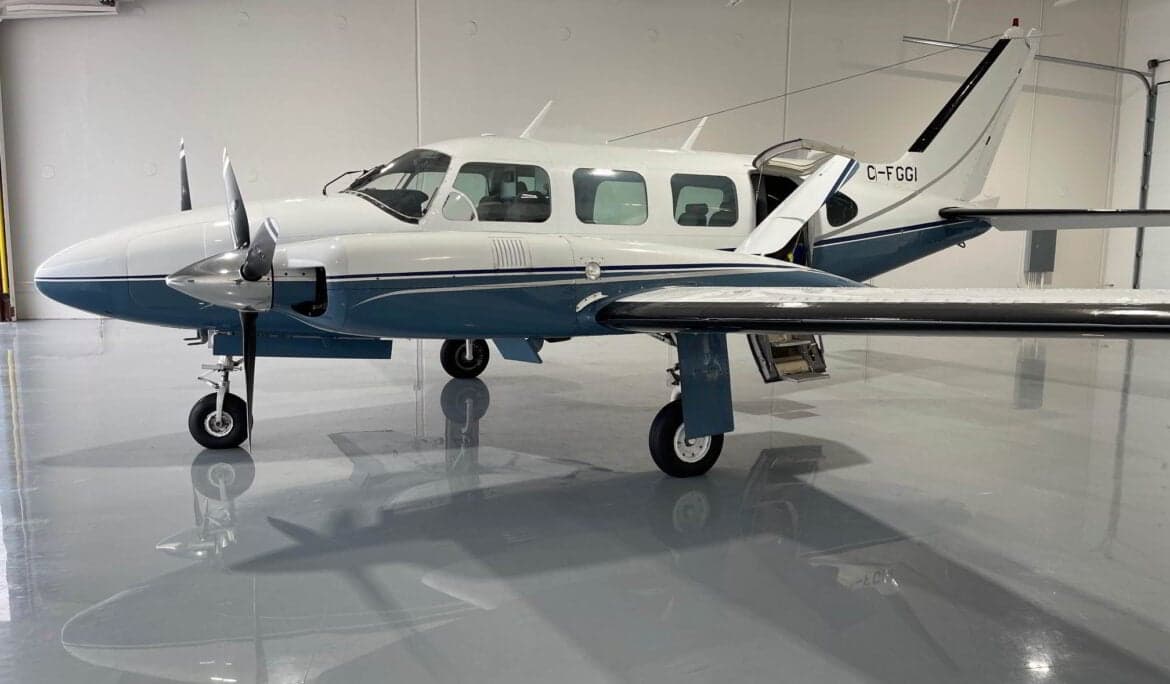 A Piper PA-31 Navajo is parked in a hangar with its door open.