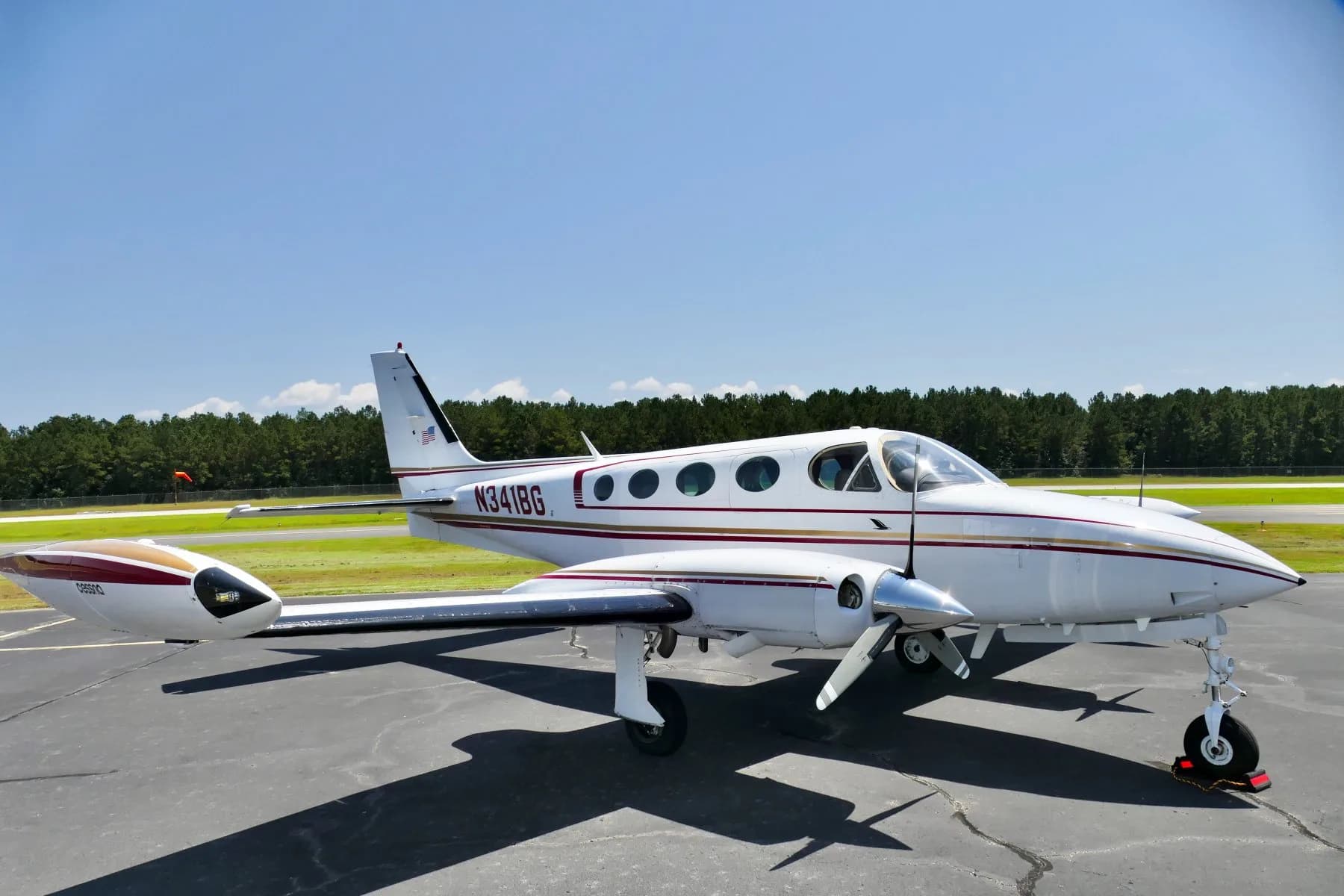 Three-quarter front view of a white twin-engine propeller aircraft N341BG with red and gold stripes on an airfield.