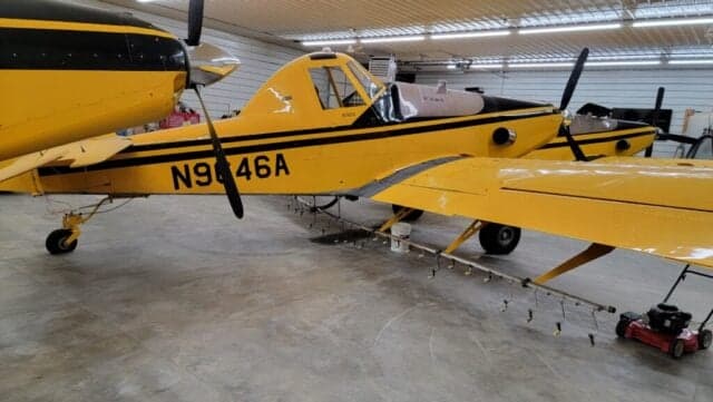 Several yellow and black aircraft parked in a hangar with lawnmowers in the foreground.