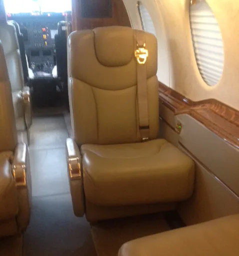 A close-up view of a single beige leather seat in an aircraft cabin.