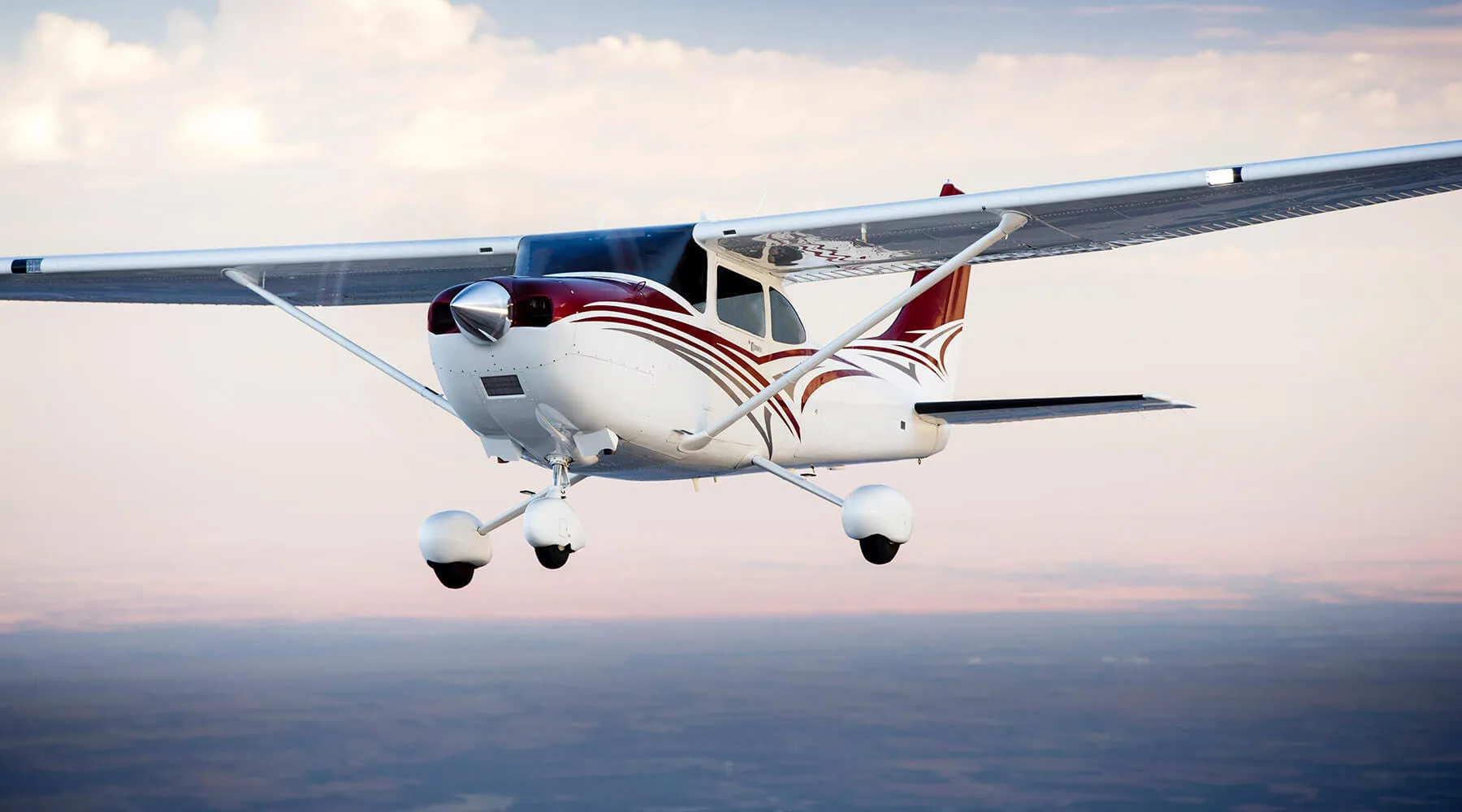 A Cessna 206 Stationair in flight, showcasing its landing gear and maroon and white paint scheme.
