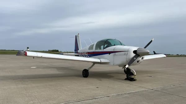 A white and blue Grumman American AA-5 Traveler parked on a concrete surface.