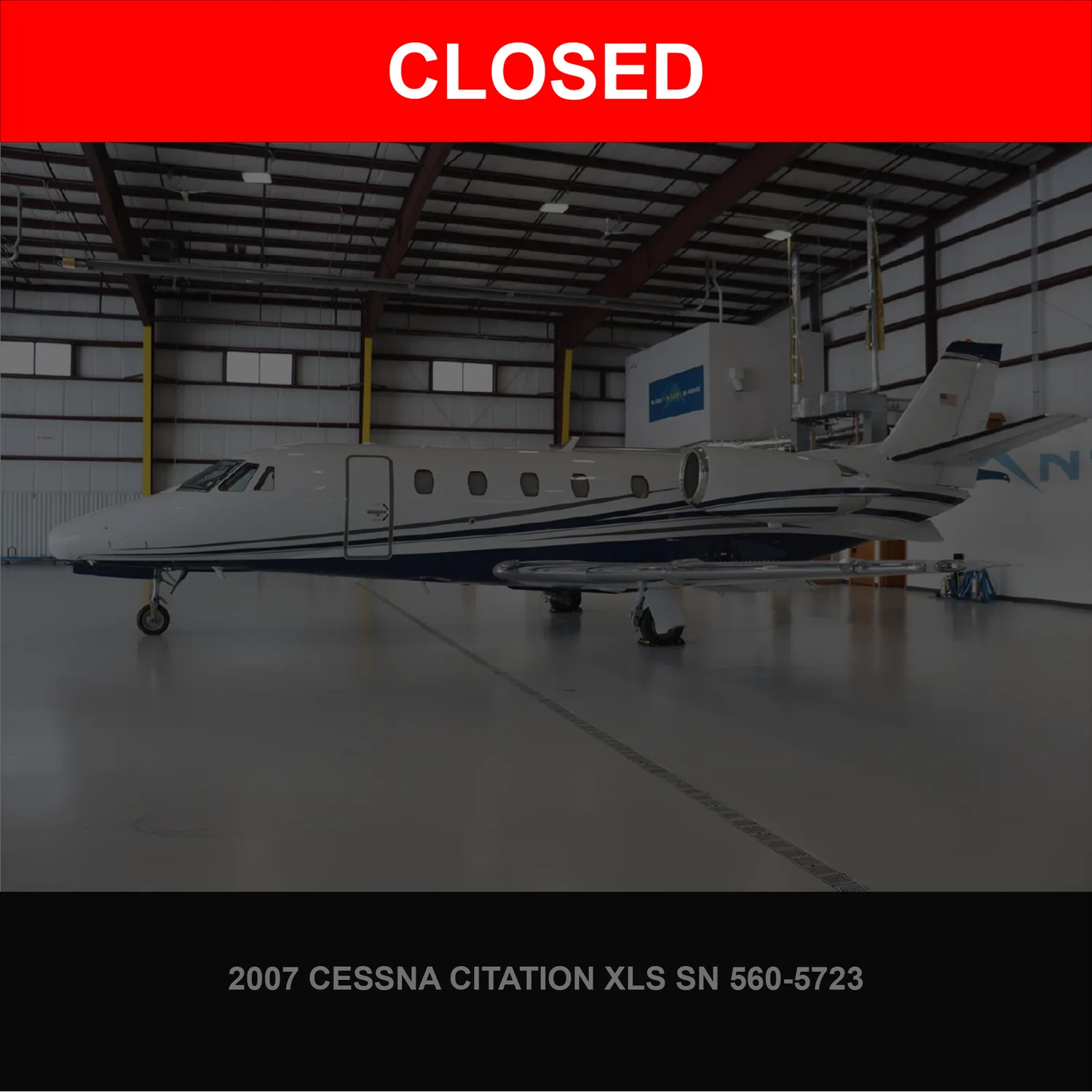 A white Cessna Citation XLS business jet with blue stripes, parked inside a hangar.
